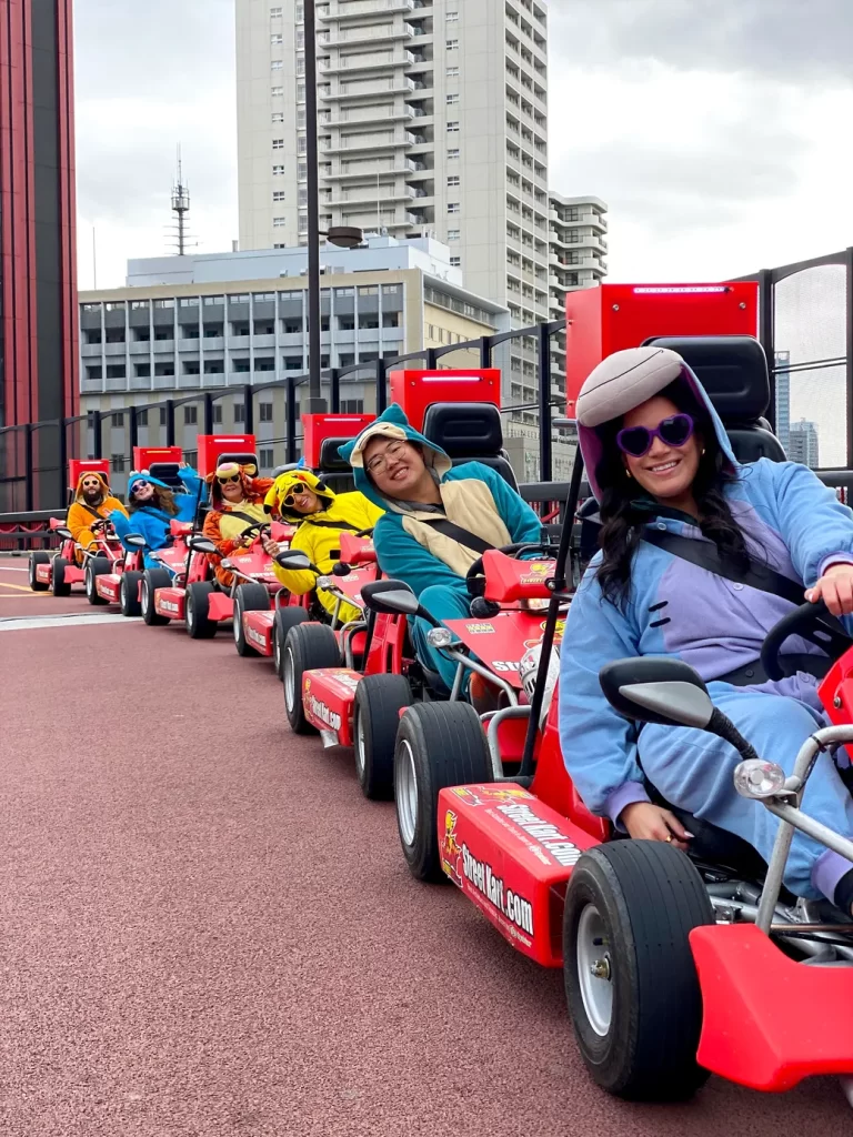 IMG_2925 - StreetKart Group of people in red go-karts lined up on an outdoor track with tall city buildings in the background.